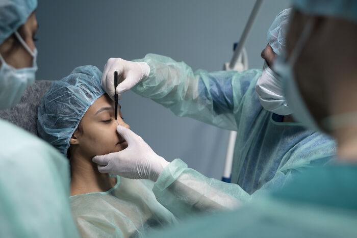 Plastic surgeons in surgical attire preparing a patient for cosmetic procedures in a clinical setting.