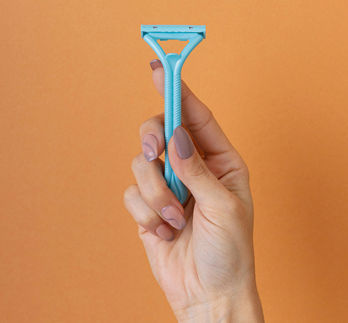 Hand holding a blue razor against an orange background, symbolizing signs people missed while being cheated on.