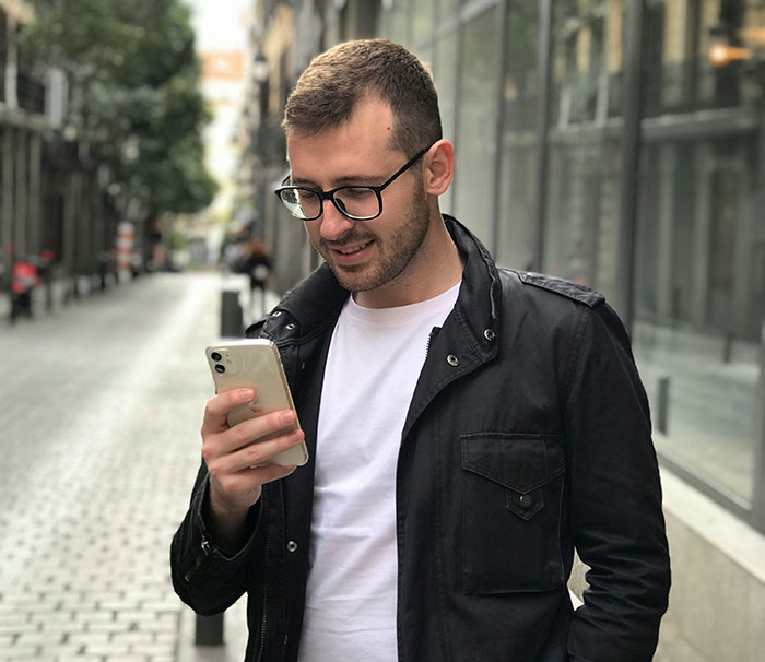 Young man in black jacket looking at phone outdoors, representing signs of pulling away in relationships and missed cheating clues.