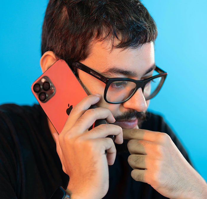 Young man wearing glasses, deep in thought while talking on phone, symbolizing signs of pulling away in relationships.