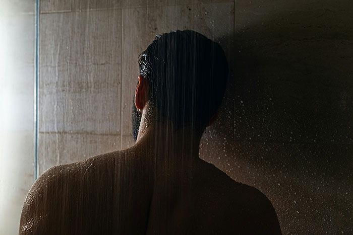 Man standing alone in a dark shower, reflecting on signs he missed while being cheated on in a relationship