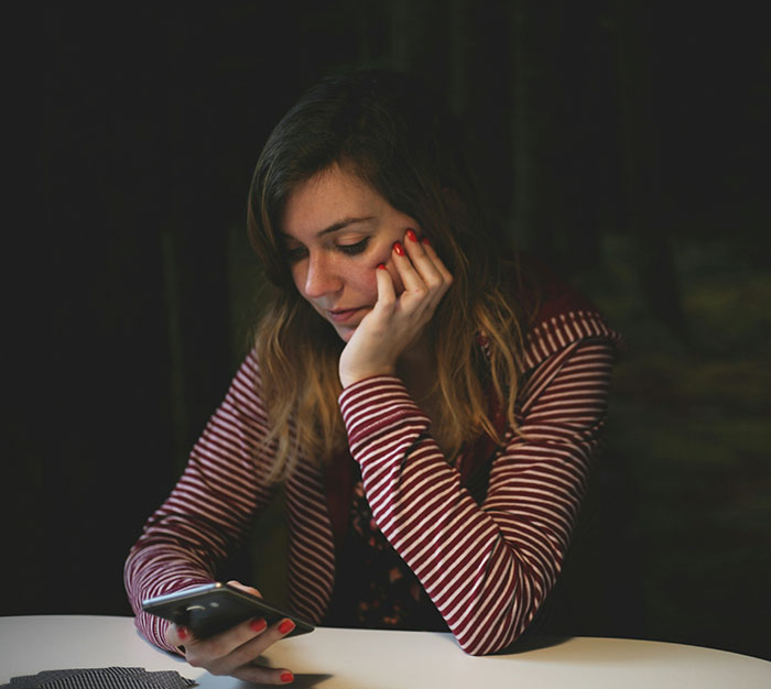 Young woman looking thoughtfully at her phone, reflecting on signs she missed while being cheated on in a relationship.