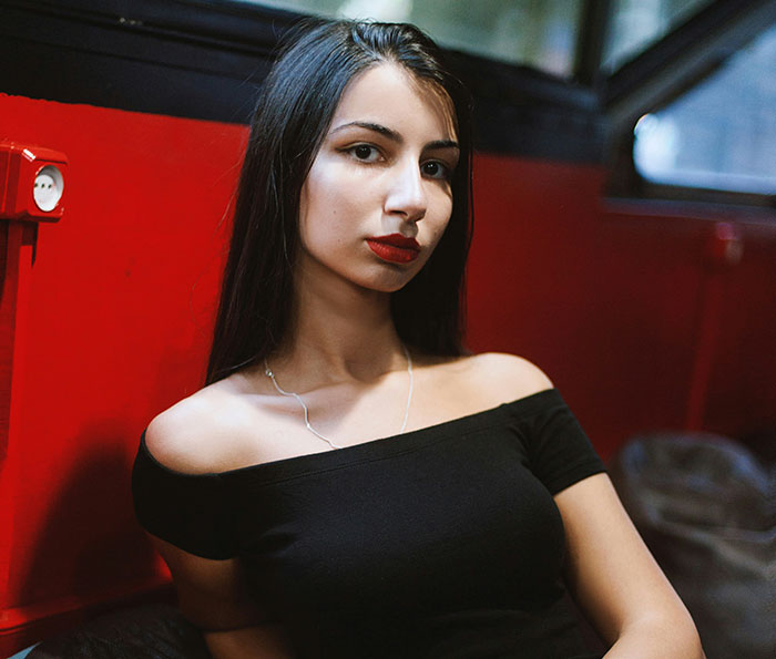 Young woman with long dark hair and red lipstick sitting indoors, reflecting on signs of being cheated on and pulling away.