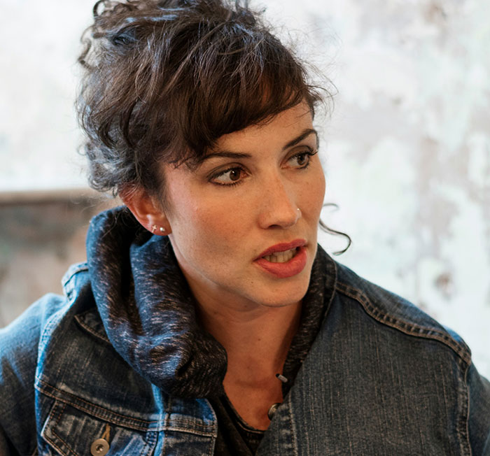 A woman with curly hair in a denim jacket looks away, expressing concern while discussing signs of being cheated on.
