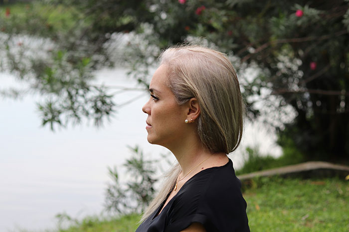 Woman with long blonde hair sitting outdoors by water, appearing thoughtful and reflective about signs of being cheated on.
