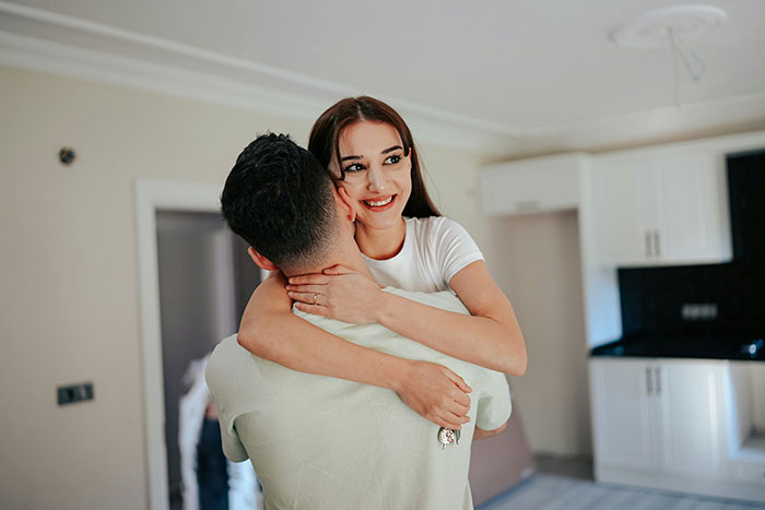 A woman smiling and hugging a man in a kitchen, illustrating signs of pulling away and missed cheating signs.