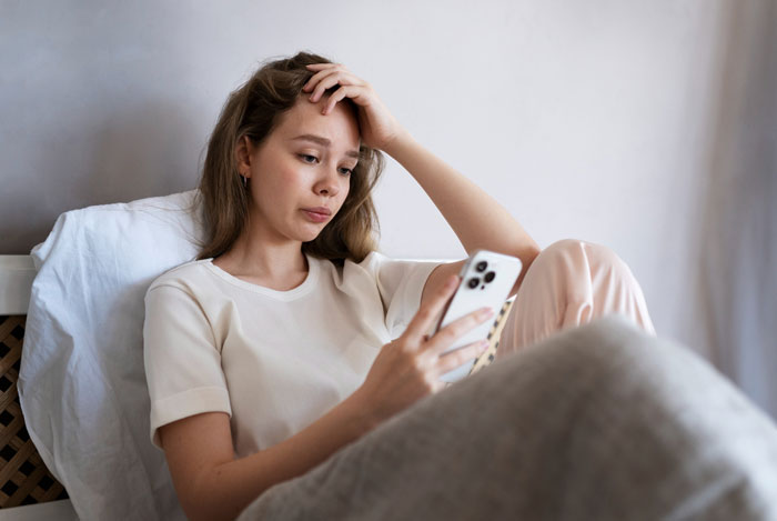 Sad 11-year-old girl sitting on bed, looking stressed while using smartphone during her birthday celebration. Sad 11-year-old girl sitting on bed, looking stressed while using smartphone during her birthday celebration.