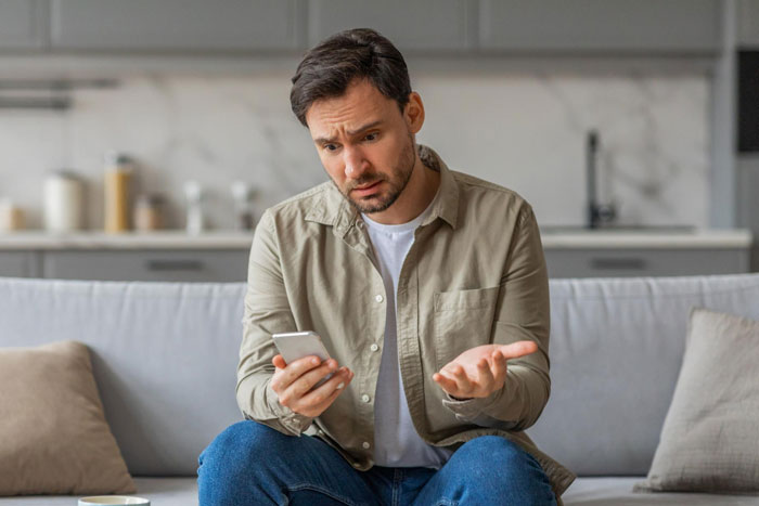 Man looking frustrated sitting on couch holding phone, representing girl’s 11th birthday visiting relatives demands. Man looking frustrated sitting on couch holding phone, representing girl’s 11th birthday visiting relatives demands.