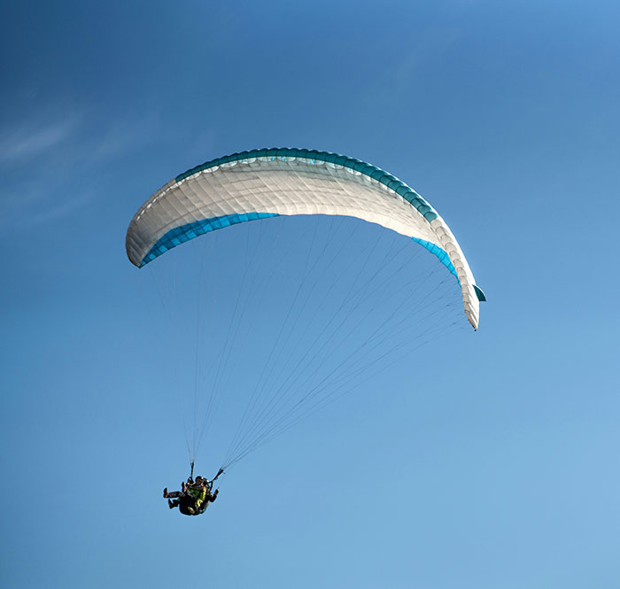 Experienced skydiver with over 400 flights descending under a parachute against a clear blue sky.