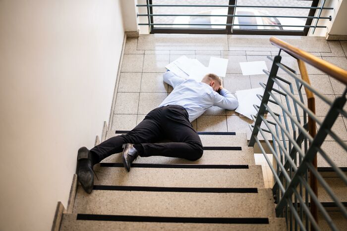 Man dressed in business attire lying unconscious on stairs surrounded by scattered papers, illustrating deadly casual accidents.