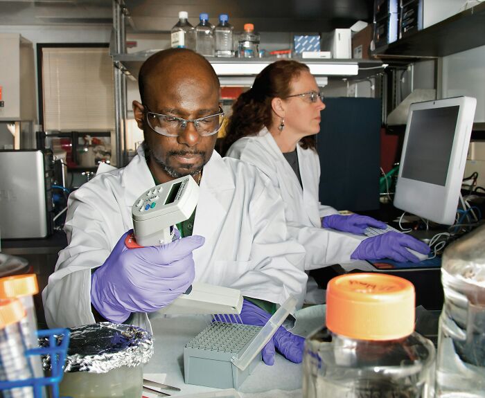 Two scientists wearing lab coats and gloves working with lab equipment in a research setting focused on genetics.