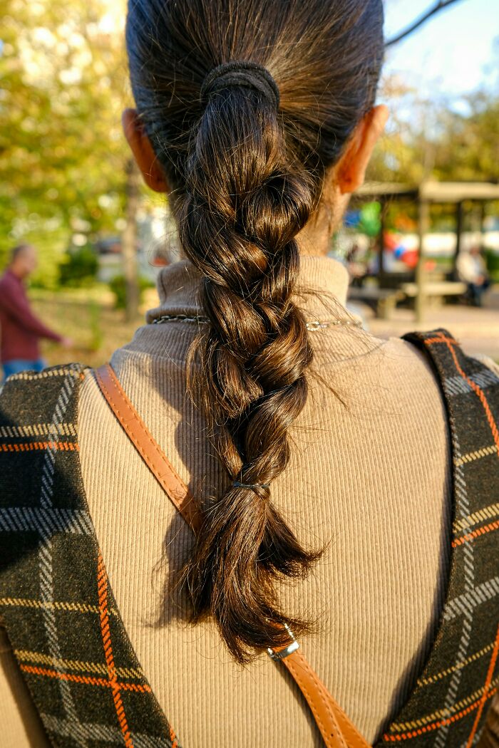 Close-up of a woman with shiny, thick braided hair showcasing unique genetic traits in natural outdoor light.