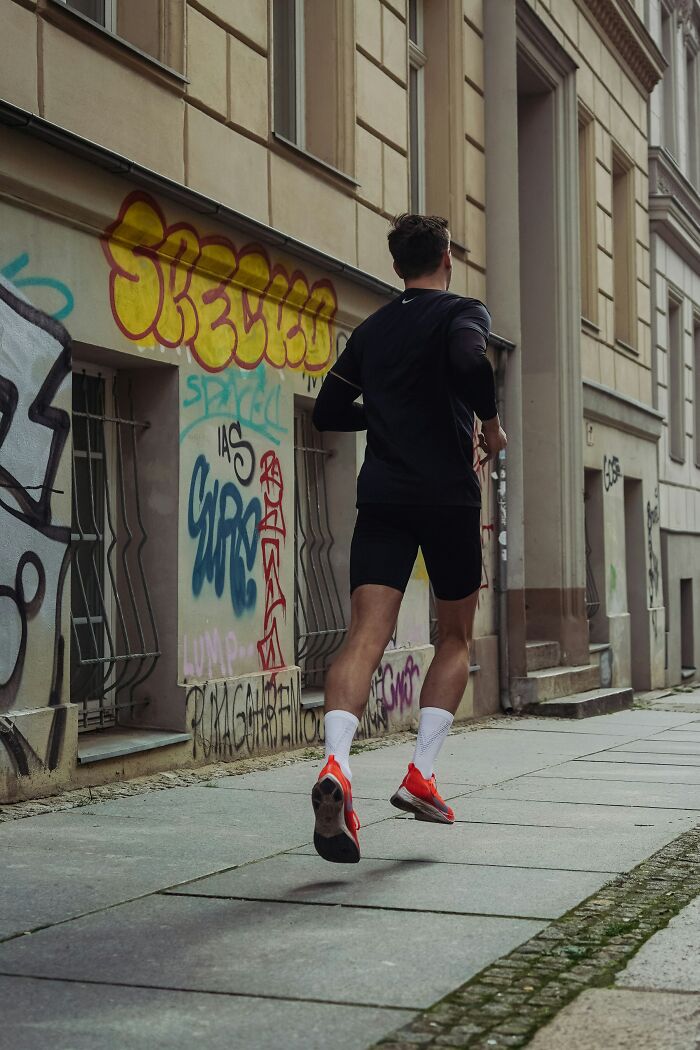 Man jogging in black athletic wear and bright sneakers along a graffiti-covered urban street, showcasing genetic lottery fitness.