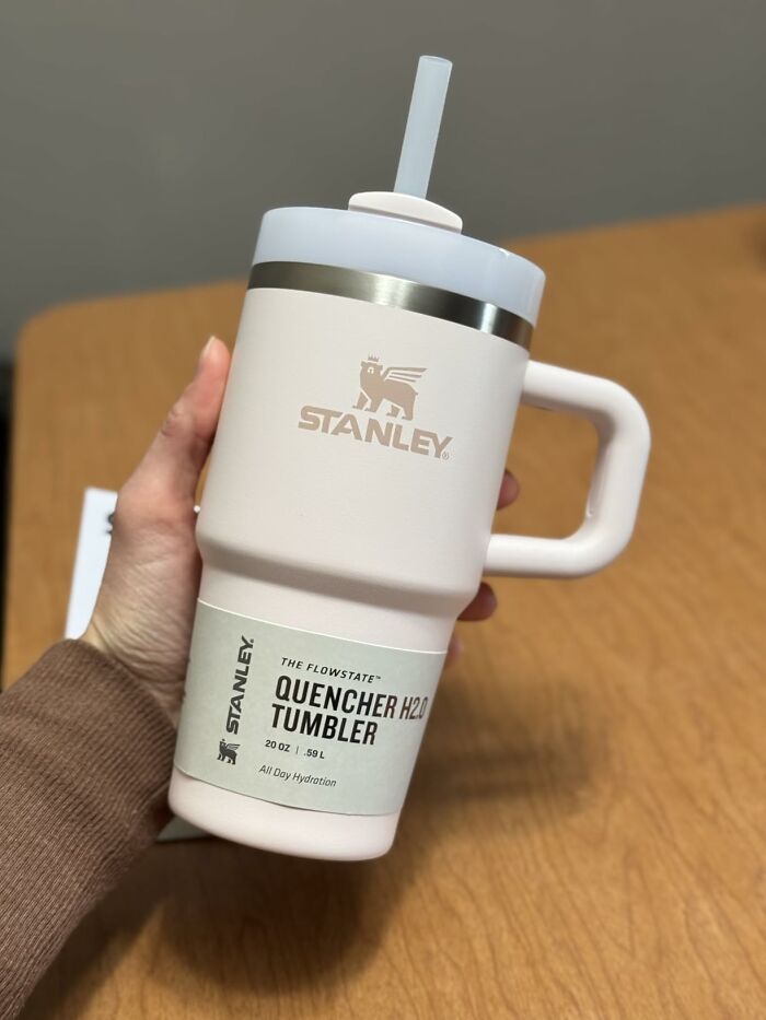 Hand holding a Stanley Quencher H2O Tumbler on a wooden table, one of the affordable finds on Amazon.