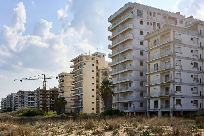 Abandoned tourist destination with empty, deteriorating high-rise buildings and overgrown vegetation under a cloudy sky.