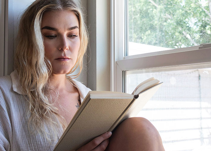 Woman over 30 reading a book by the window, reflecting on things women stopped pretending they like after 30.