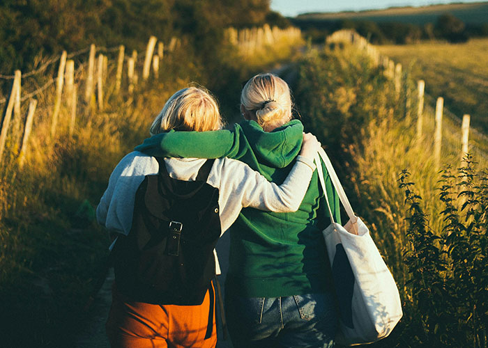 Two women walking outdoors in casual clothes, embracing each other, reflecting things women stopped pretending to like after 30.