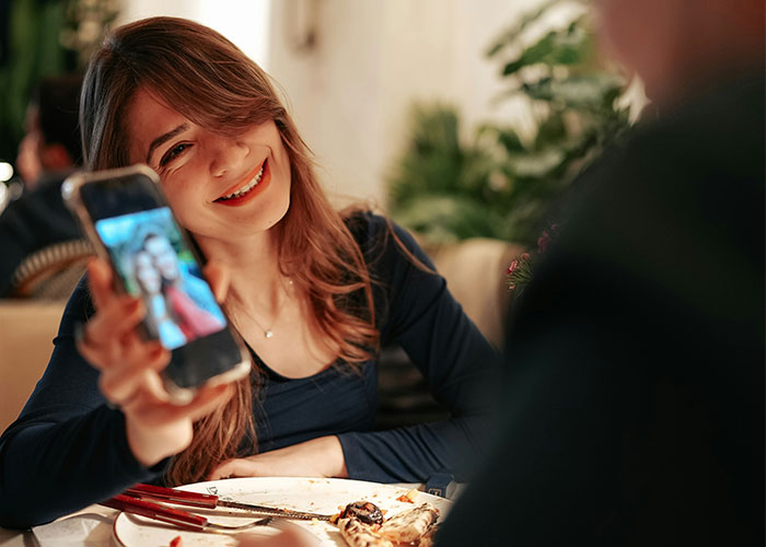 Young woman smiling at a restaurant showing a selfie on her phone, reflecting changes women stopped pretending they like after 30