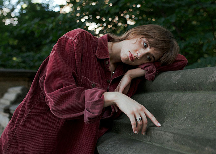 Young woman in a red shirt leaning on a stone surface, reflecting on things women stopped pretending to like after 30.