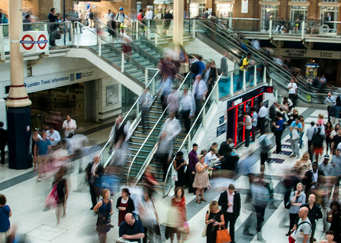 Busy crowd inside a London train station with people moving near escalators and information signs, reflecting urban lifestyle.