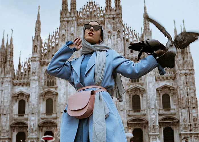 Woman in stylish blue coat and sunglasses with pigeons in front of a historic building, reflecting things women stopped liking after 30.