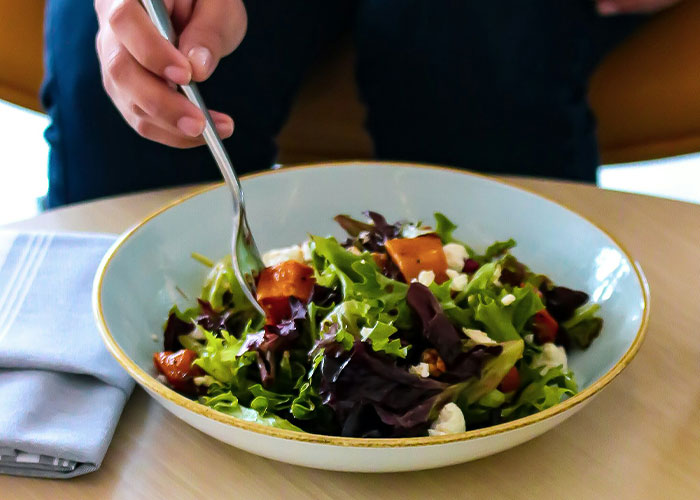 Woman eating a fresh salad with mixed greens and roasted vegetables, illustrating things women stopped pretending they like after 30.
