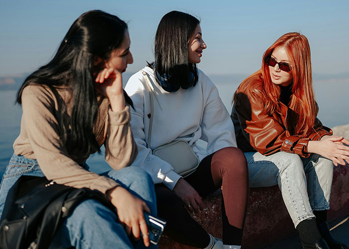 Three women in casual outfits sitting outdoors by the water, reflecting changes women stopped pretending they like after 30.