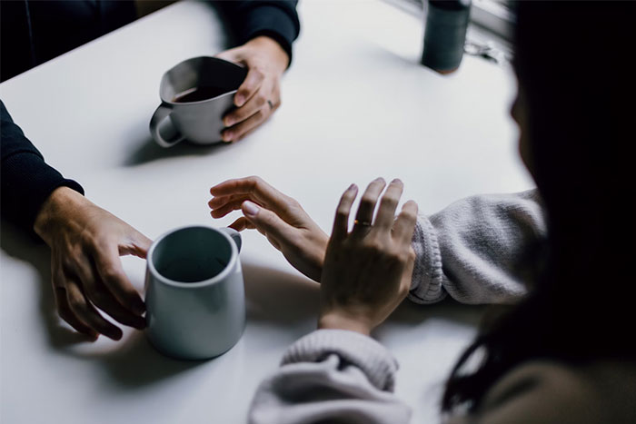 Two people talking over coffee, one reaching out as if to stop a proposal during a wedding conversation.