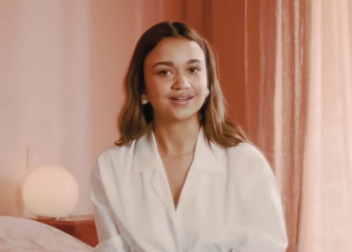 Young woman sharing stories about people who knew celebrities before fame in a softly lit room with warm tones.