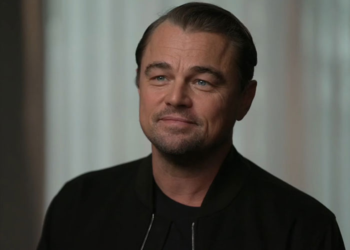 Man with slicked-back hair and black jacket smiling softly in an interview about people who knew celebrities before fame reveals