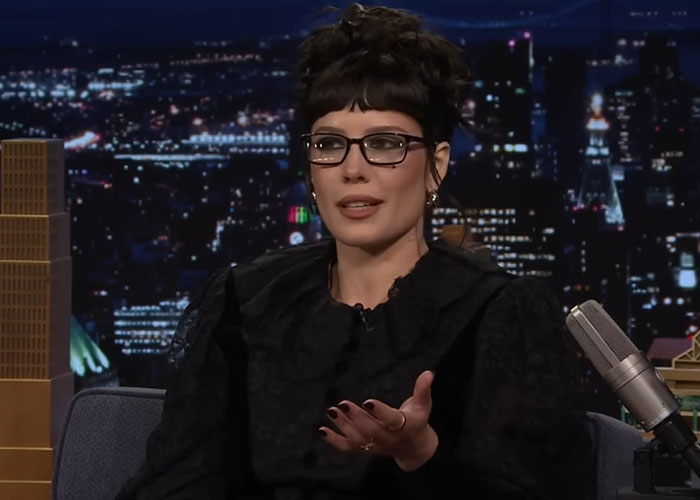 Woman wearing glasses and a black outfit sharing stories on a late night talk show about people who knew celebrities before fame