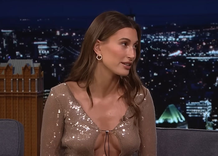 Young woman wearing a sparkly top speaking on a late night show, sharing stories about people who knew celebrities before fame