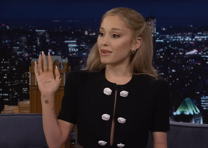 Woman with tattoos raising her hand during a late-night talk show, revealing what people who knew celebrities before fame say.
