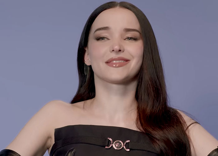 Young woman with long dark hair smiling confidently against a solid background, sharing stories from people who knew celebrities before fame.