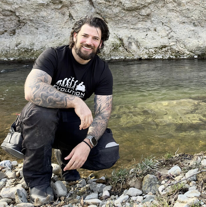 Actor known for playing Viktor Krum in Harry Potter crouching by a riverbank with tattoos on his arms and smiling