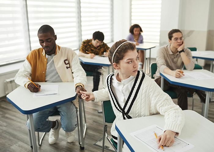 Students in classroom taking different quiz versions while teacher catches cheaters by handing out 24 quiz variations.