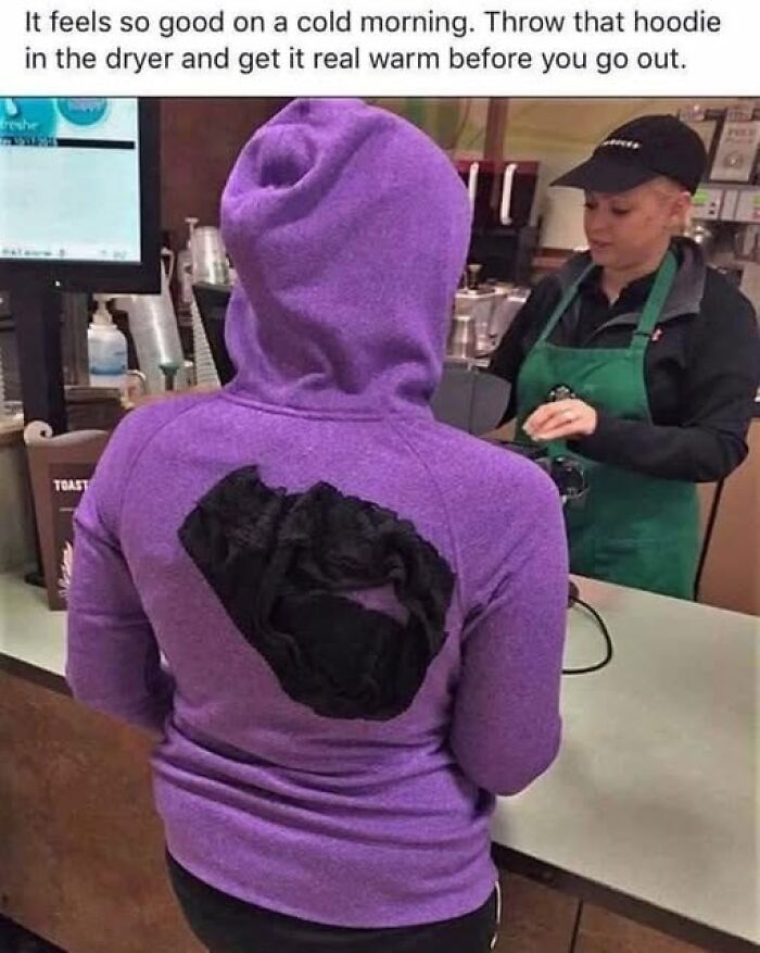 Person wearing a purple hoodie with a funny black stain on the back, standing at a coffee shop counter with a barista.