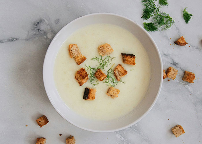 Bowl of creamy soup garnished with herb sprigs and toasted bread cubes, illustrating dark family secrets concept.