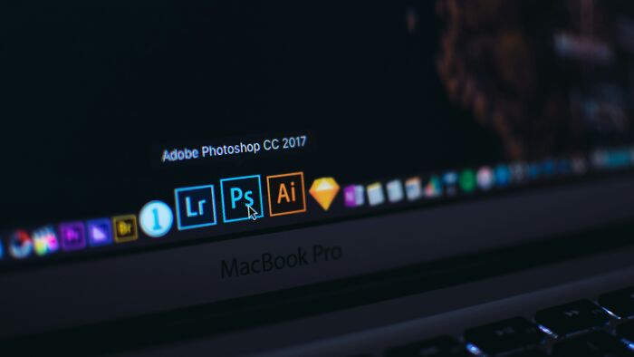 Close-up of MacBook Pro screen showing Adobe Photoshop and design apps, representing people share companies bad list context.
