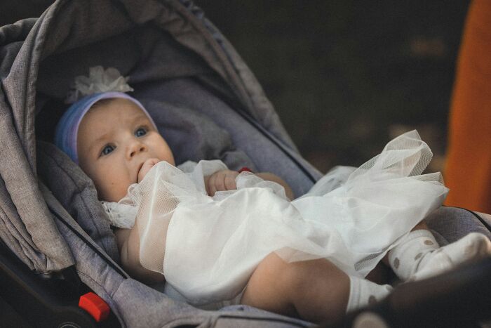Baby dressed in white sitting in a stroller, illustrating hilariously bad names that made people question parenting choices.