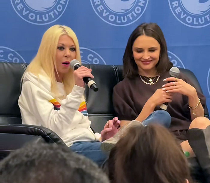 Two women speaking at a panel, with one holding a microphone, related to American Pie star recent interview appearance. Two women speaking at a panel, with one holding a microphone, related to American Pie star recent interview appearance.