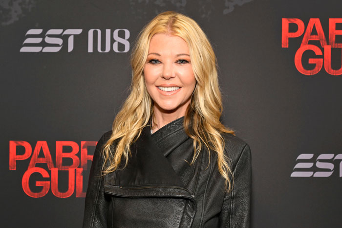 Female American Pie star with long blonde hair wearing a black jacket, smiling at a red carpet event. Female American Pie star with long blonde hair wearing a black jacket, smiling at a red carpet event.