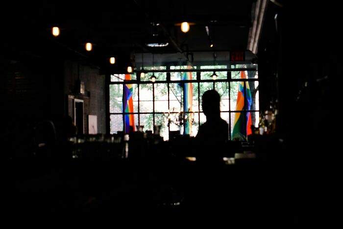 Silhouetted bartender behind a dimly lit bar with colorful flags in the background showing bartender stories.