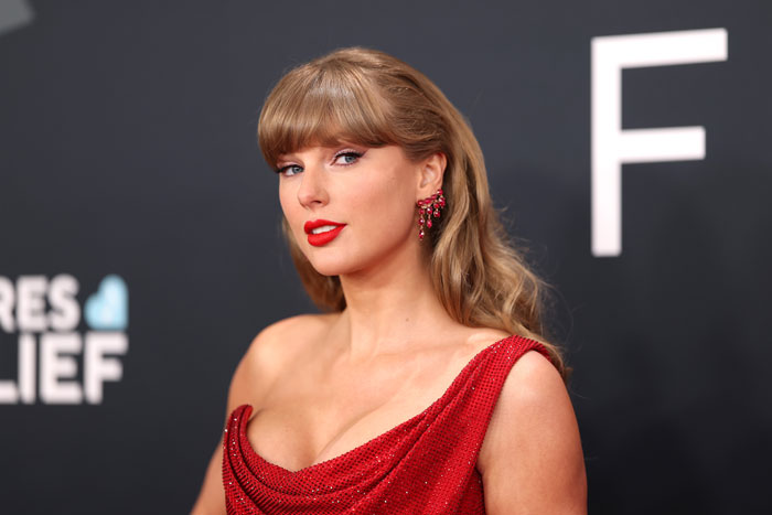 Taylor Swift in a red dress and earrings, posing on a black carpet event amid Trump claims about her image.