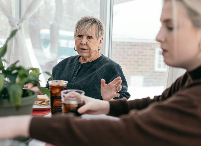 Older woman speaking seriously to younger pregnant woman during tense playdate conversation at home.