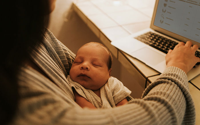 Man wonders if he&rsquo;s a jerk while holding sleeping baby and working on laptop at home during family time.
