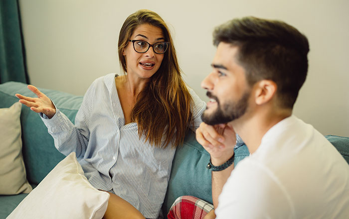 Man and woman having a serious conversation at home, reflecting on dad wondering if he&rsquo;s a jerk for not joining work trip with kids