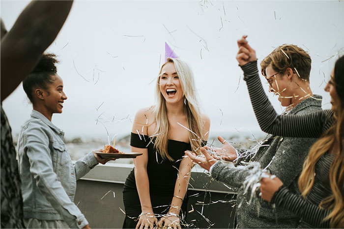 Group of friends celebrating with party hats and confetti, highlighting reactions to terrible gifts from partners at a rooftop event.