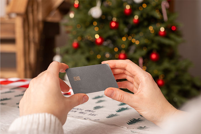 Hands holding a card near a decorated Christmas tree, illustrating gifts from partners as a red flag in relationships.