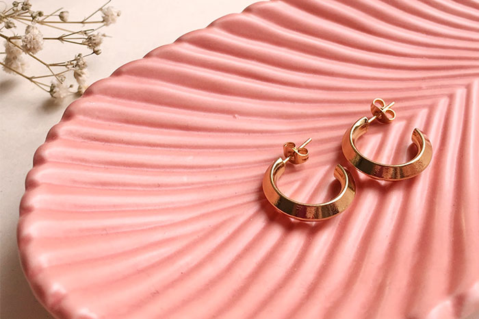 Gold hoop earrings on a pink textured dish, representing gifts from partners as a red flag in relationships.
